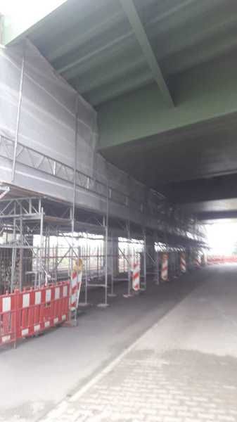 Gerüstlage entlang des Trägers, Absperrung zur Fahrbahn, Zugang über die Stirnseite der Anlage.